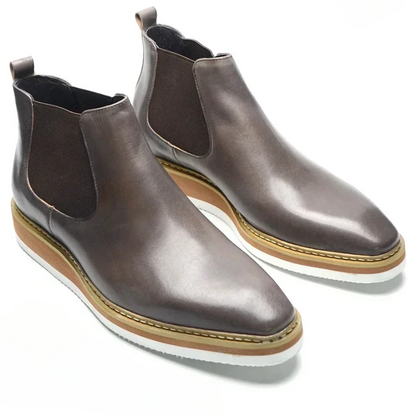 Pair of brown leather Chelsea boots with a white sole on a white background