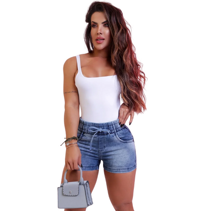 Woman wearing a white tank top and blue denim shorts, holding a small gray handbag on a white background.
