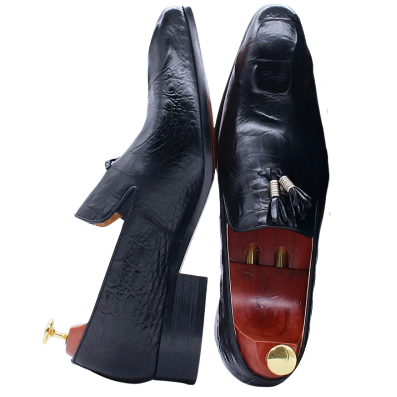 Pair of black leather dress shoes with gold accents on a white background